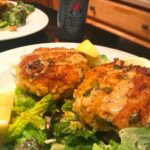 Two golden crab cakes on salad with lemon